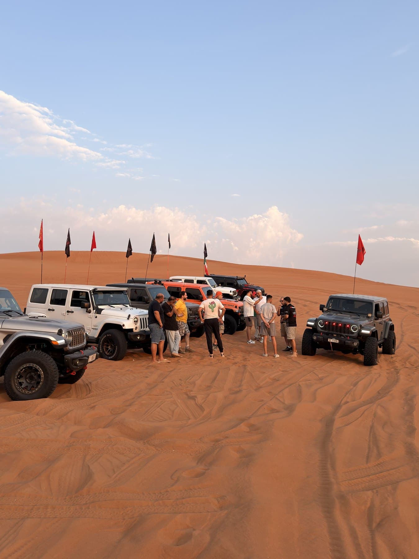 Members gathered beside their Jeeps on a dune, club flags flying