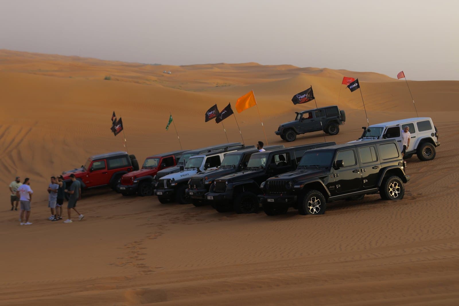 Jeeps parked across the dunes with club flags flying at sunset