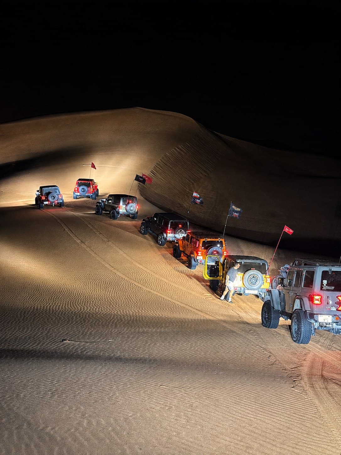Jeeps strung out across a floodlit dune at night