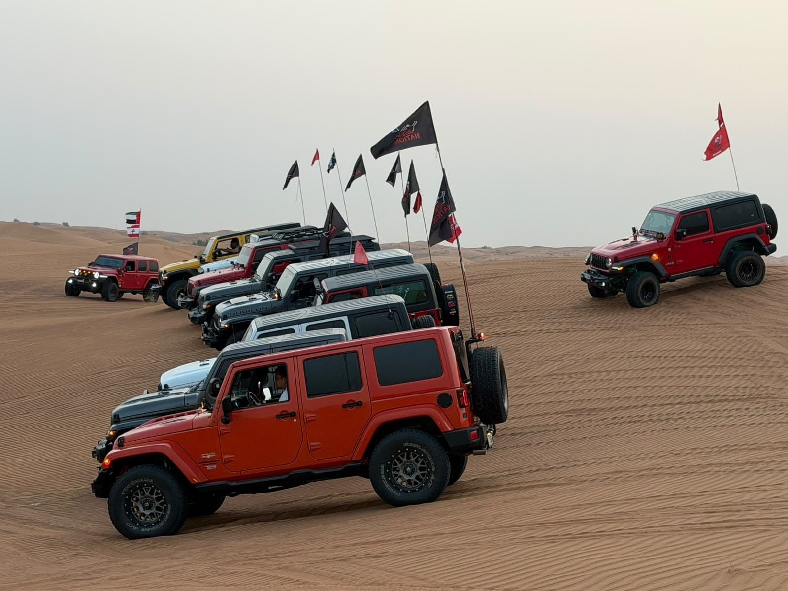 A red Jeep leading a flagged convoy through the dunes